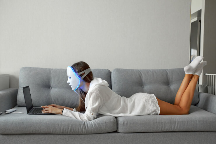 LEDマスクを頭にのせた美少女が自宅でノートパソコンに向かっている。