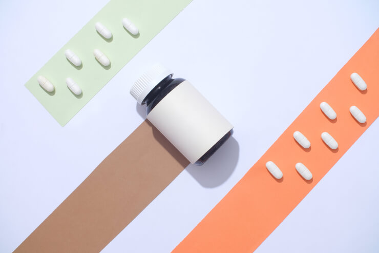 色の帯と白い錠剤を背景に、ラベルのない薬瓶が表示されている